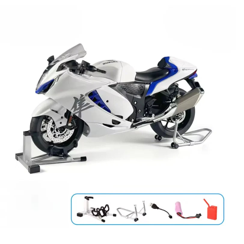 Miniature moto Suzuki Hayabusa 1/6 blanche avec accessoires visibles : béquilles latérales, batterie, prise de recharge et compartiment pour remplir l’eau pour le système de fumée, illustrant les fonctionnalités avancées.